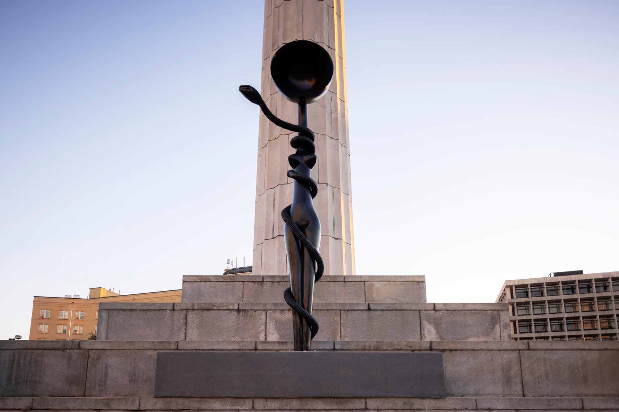 A public art piece, "Sentinel," stands in an outdoor, New Orleans city scene, in front of a blue sky.