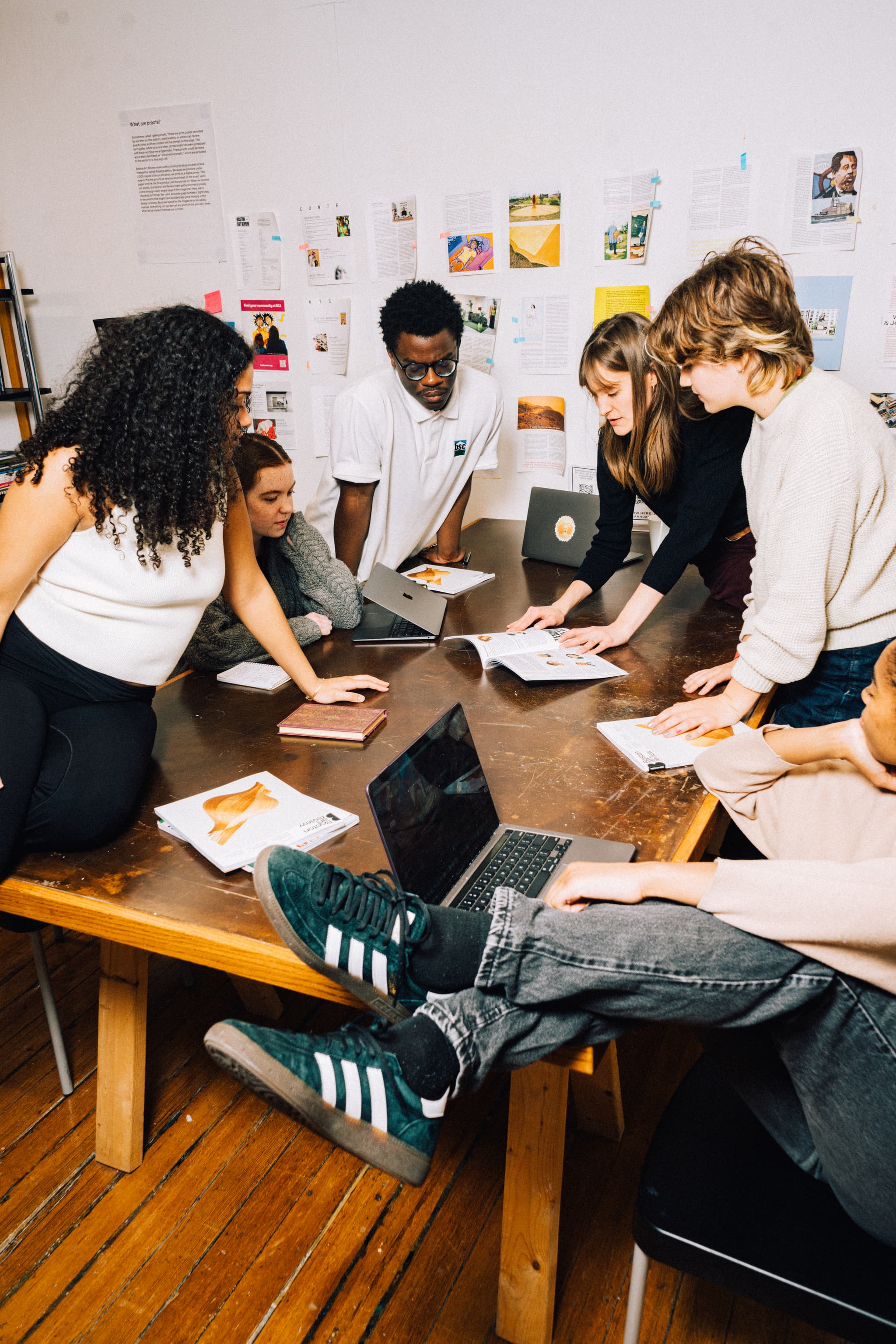Boston Art Review team gathered around a table, all inspecting a copy of Issue 11: Emerge.